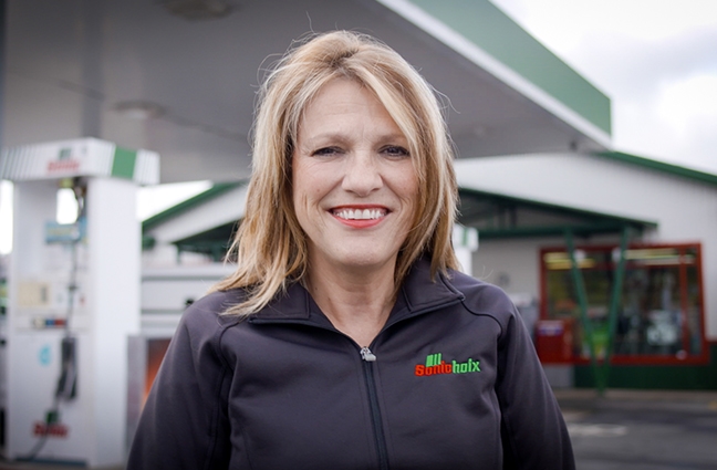 A smiling woman in front of a gas station